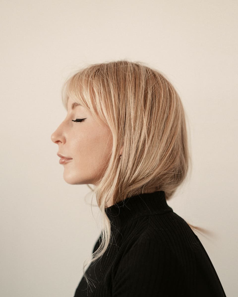 Profil d’une femme aux yeux clos, carré blond effilé et frange légère, col roulé noir